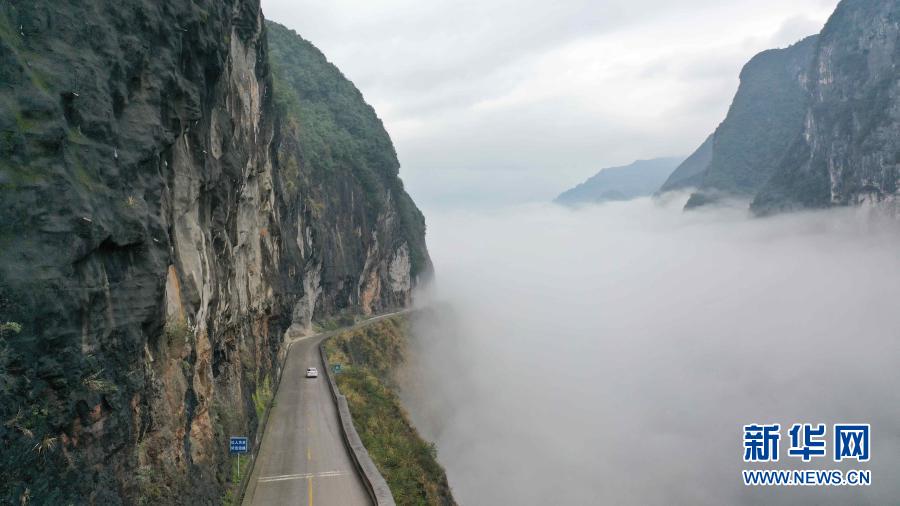 11月18日，車輛行駛在湖北省鶴峰縣的雕崖公路上。雕崖公路位于湖北省恩施土家族苗族自治州鶴峰縣境內(nèi)，全長約3公里，是巴鶴（巴東縣至鶴峰縣）公路中的一段。這里峽谷深臥、絕壁聳峙、云霧繚繞。雨后初晴，車行雕崖公路上宛如穿行在云霧中，成為一道美麗的風(fēng)景線。新華社發(fā)（楊順丕 攝）
