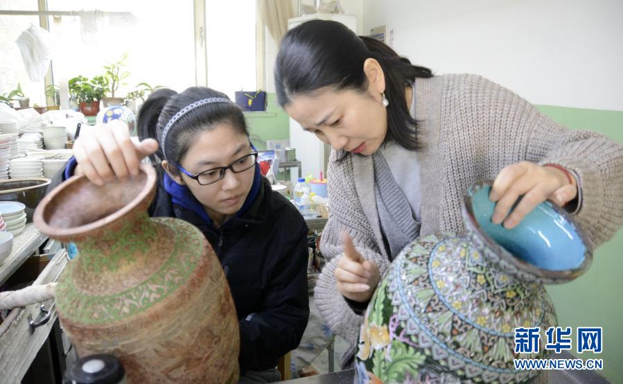 12月2日，景泰藍(lán)技藝國家二級點(diǎn)藍(lán)技師聾啞人趙楠（右）在用手語指導(dǎo)她的徒弟劉鳴燕昊。從2005年起，北京琺瑯廠有限責(zé)任公司開始招收聾啞人技工，經(jīng)過老技師們的精心培養(yǎng)，目前有17位聾啞人成為景泰藍(lán)技師，有些還成為景泰藍(lán)技藝國家二級技師。通過學(xué)習(xí)景泰藍(lán)技藝，這些聾啞人在無聲的世界里有了一個(gè)多彩的人生。新華社記者 李欣 攝