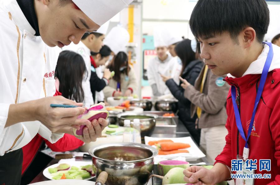 12月15日，順德廚師學(xué)院學(xué)生（左）向參賽選手展示雕花制作。新華社記者 黃國保 攝